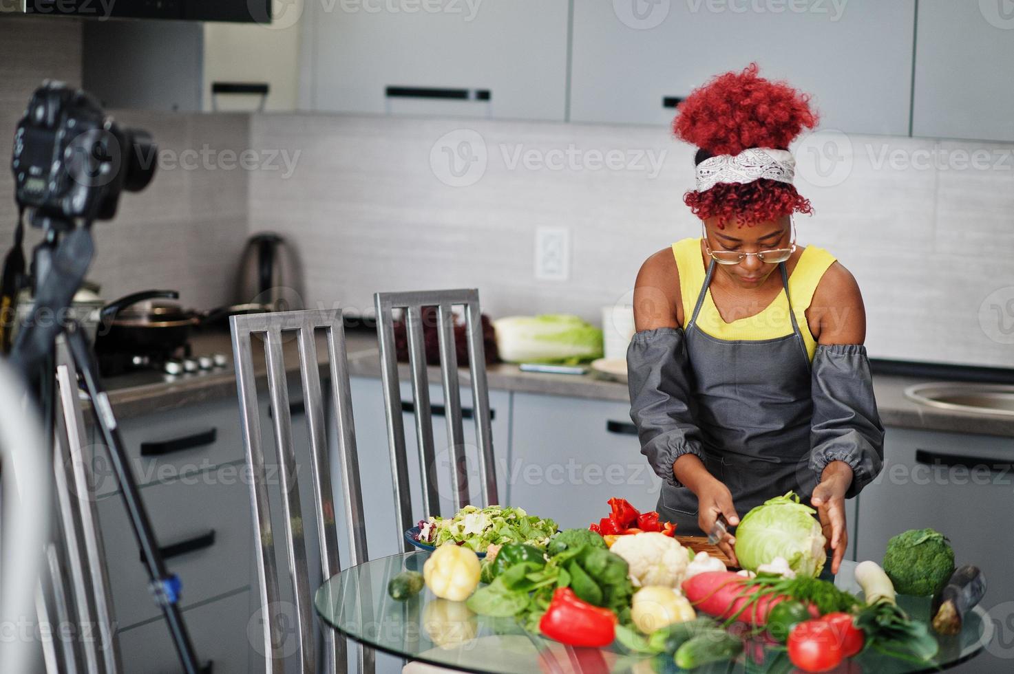 African american woman filming her blog broadcast about healthy food at home kitchen. She cuts the cabbage. photo