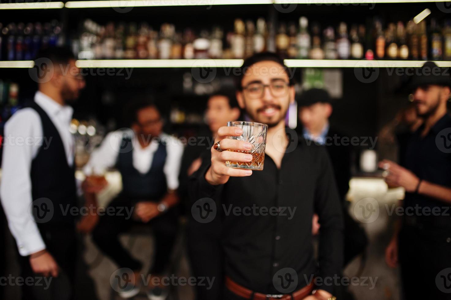 Stylish arab man against group of handsome retro well-dressed guys gangsters spend time at club, drinking on bar counter. Multiethnic male bachelor mafia party in restaurant. photo