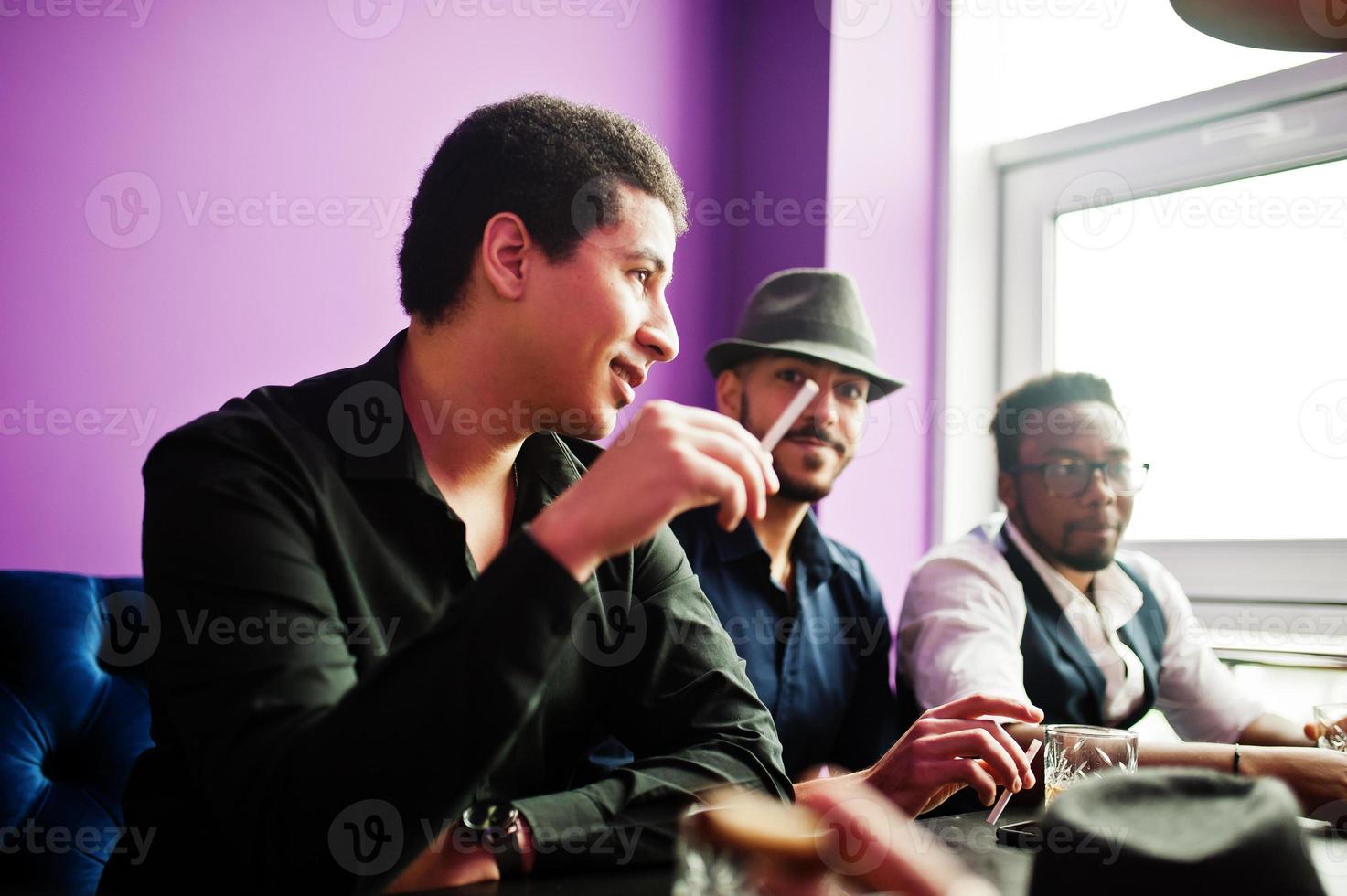 Group of handsome retro well-dressed man gangsters spend time at club, sitting and drinking whiskey. Multiethnic male bachelor mafia party in restaurant. photo