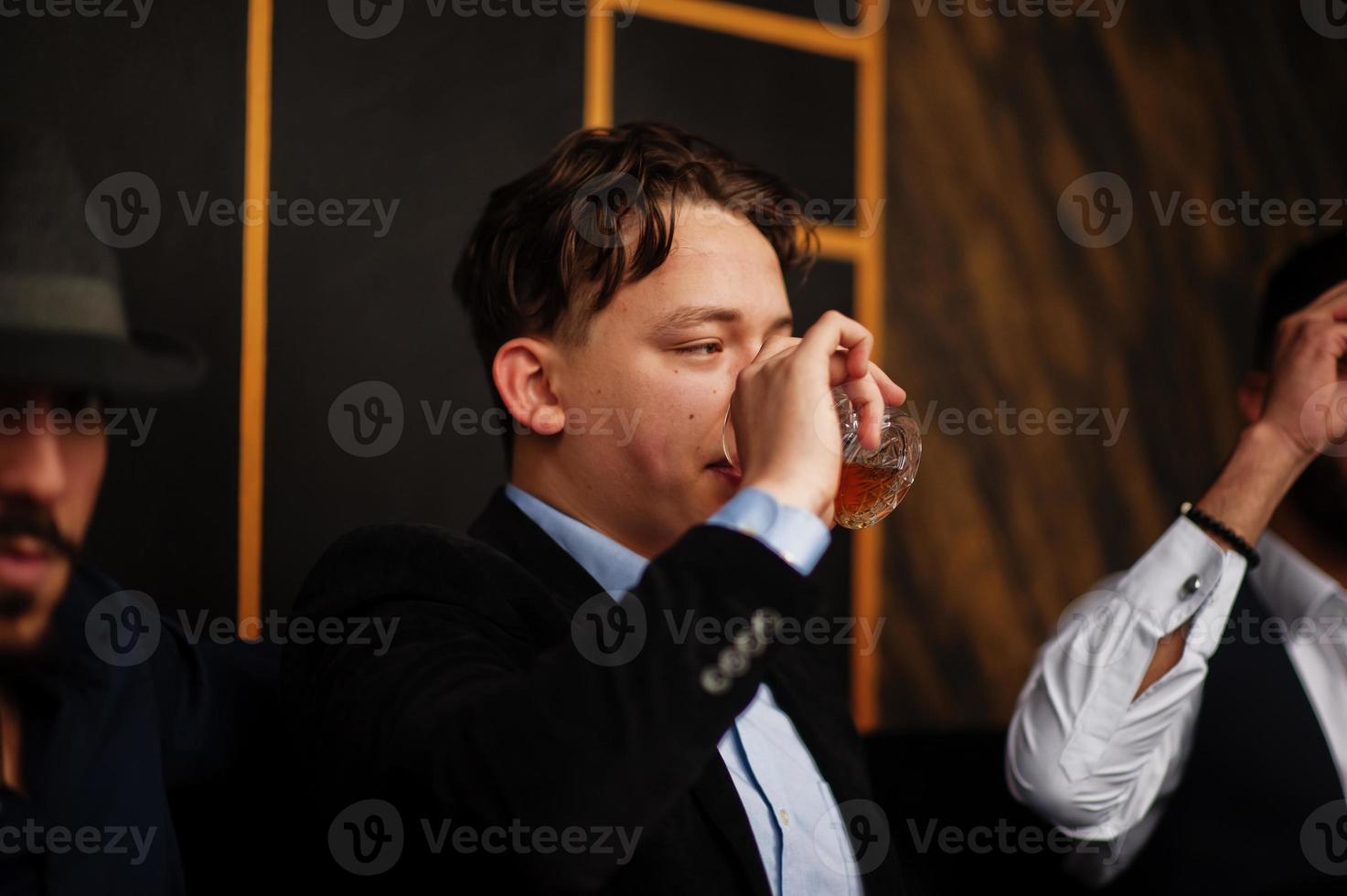 Group of handsome retro well-dressed man gangsters spend time at club, smoking hookah. Multiethnic male bachelor mafia party in restaurant. photo