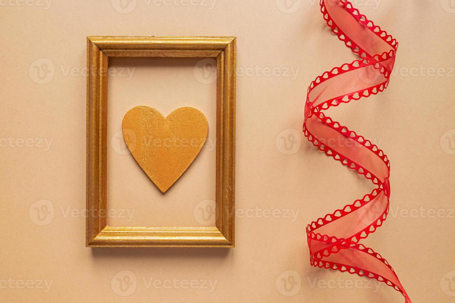 Valentine's day or Wedding romantic concept. Twisted decorative ribbon and golden photo frame with wooden heart on beige background.