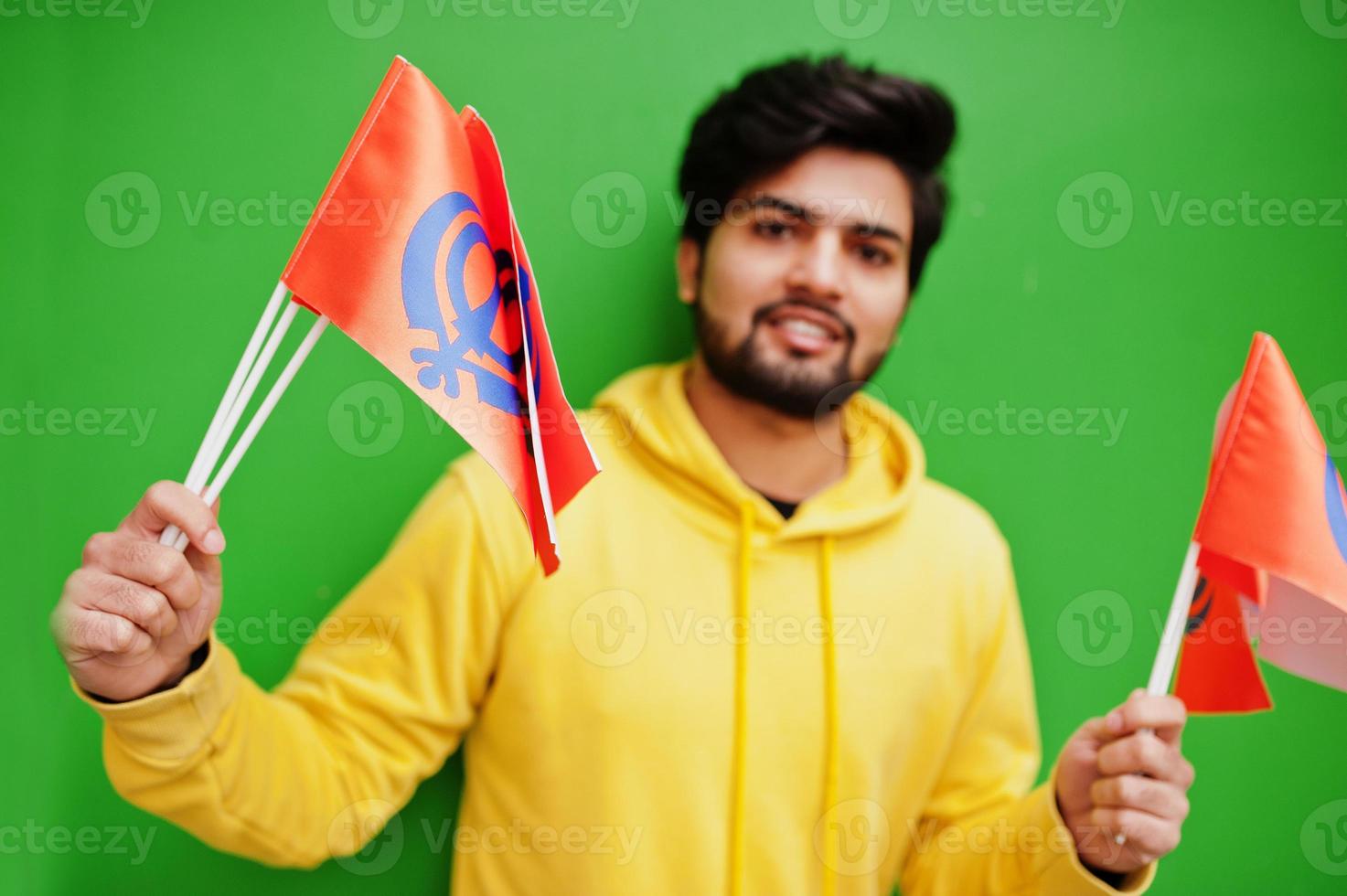 Happy Guru Nanak Jayanti concept. Young indian man in yellow sweatshirt hold flags. Cool south asian guy wear hoodie celebrating India holiday. photo