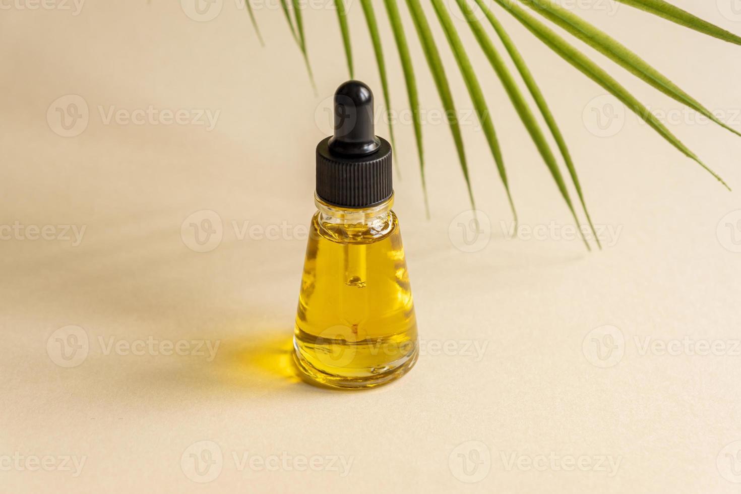 una botella cosmética de vidrio con un cuentagotas sobre un fondo gris con hojas de palma. concepto de cosmética natural, aceite esencial natural foto