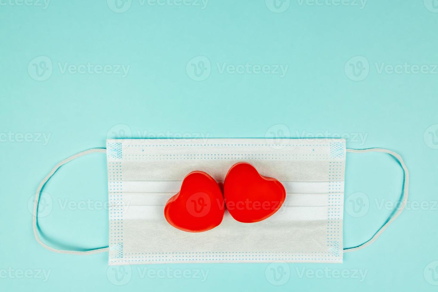 Two red hearts on medical protection mask on light blue background, top view. Concept of healthcare, self-defense. Creative flat lay with copy space photo