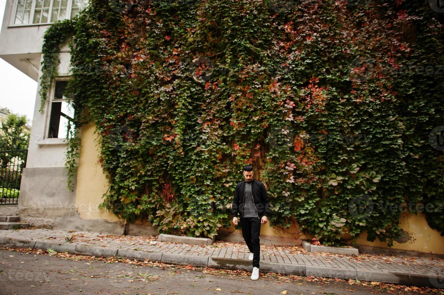 Portrait of stylish arab beard man wear grey turtleneck and black jaket. Arabian model guy on a background of autumn leaves. photo