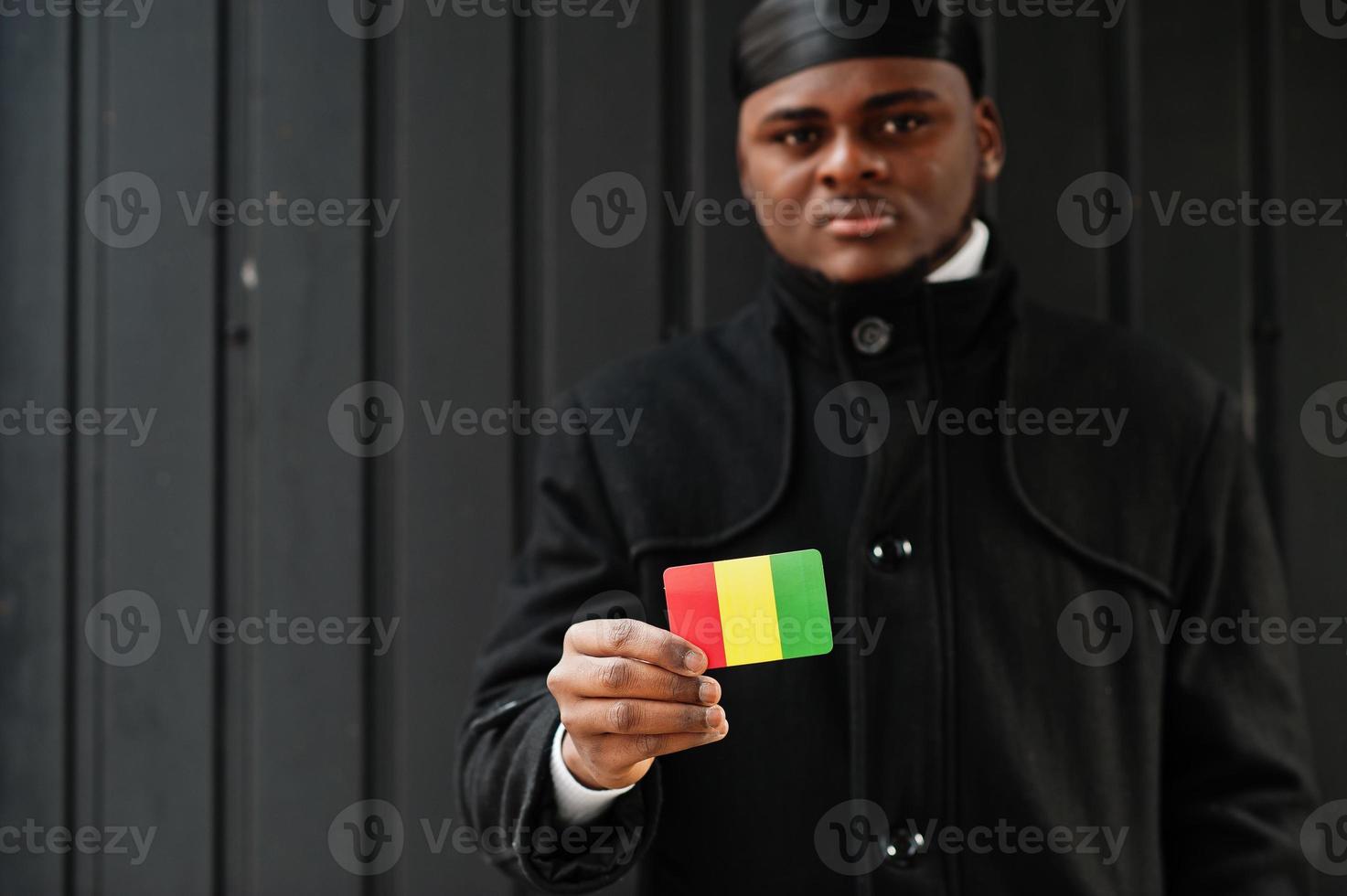 hombre africano usa durag negro sostiene la bandera de guinea a mano aislado fondo oscuro. foto