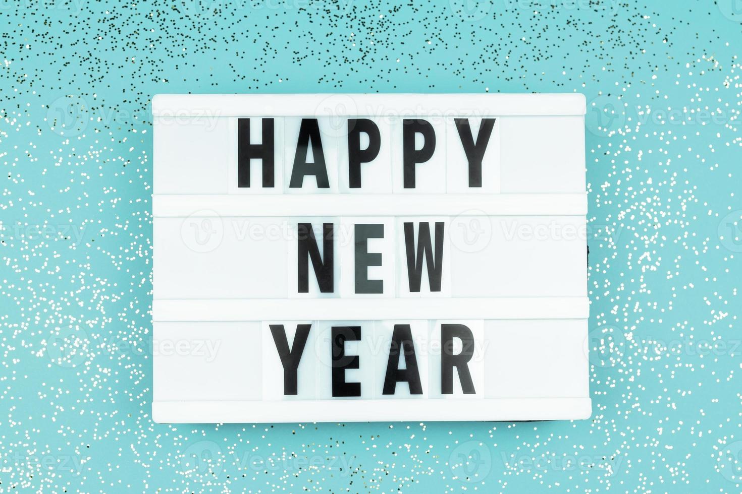 Happy new year light box with on blue background with scattered sparkling confetti. photo