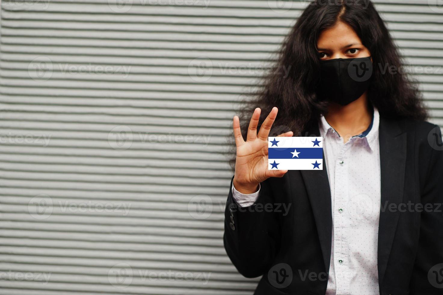 mujer asiática con ropa formal y máscara protectora negra sostiene la bandera de las islas Gambier a mano contra un fondo gris. coronavirus en el concepto de país. foto