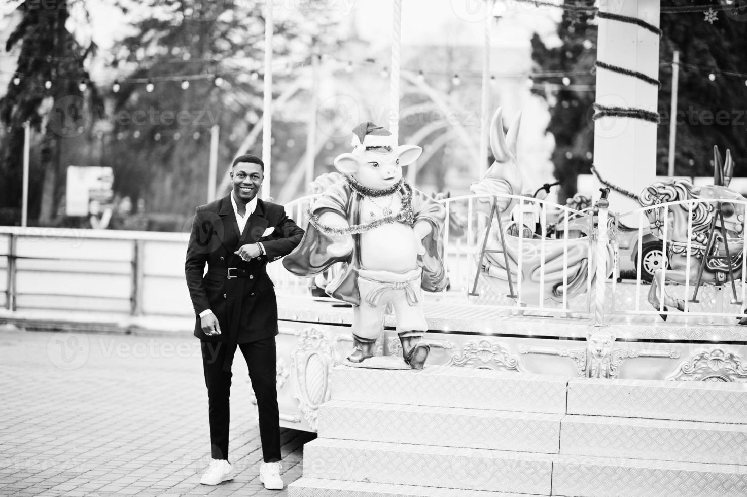 retrato de joven y guapo hombre de negocios afroamericano en traje pose atracciones de carrusel de fondo. foto