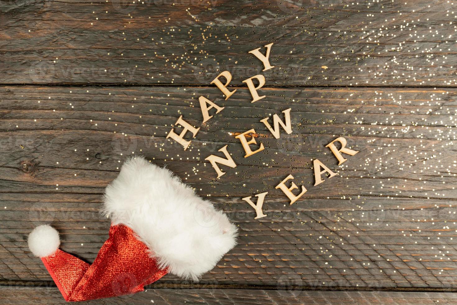 festive greeting card for new year with red santa hat and wooden text scettered out of it on a table. copy psace for text. Holiday concept photo