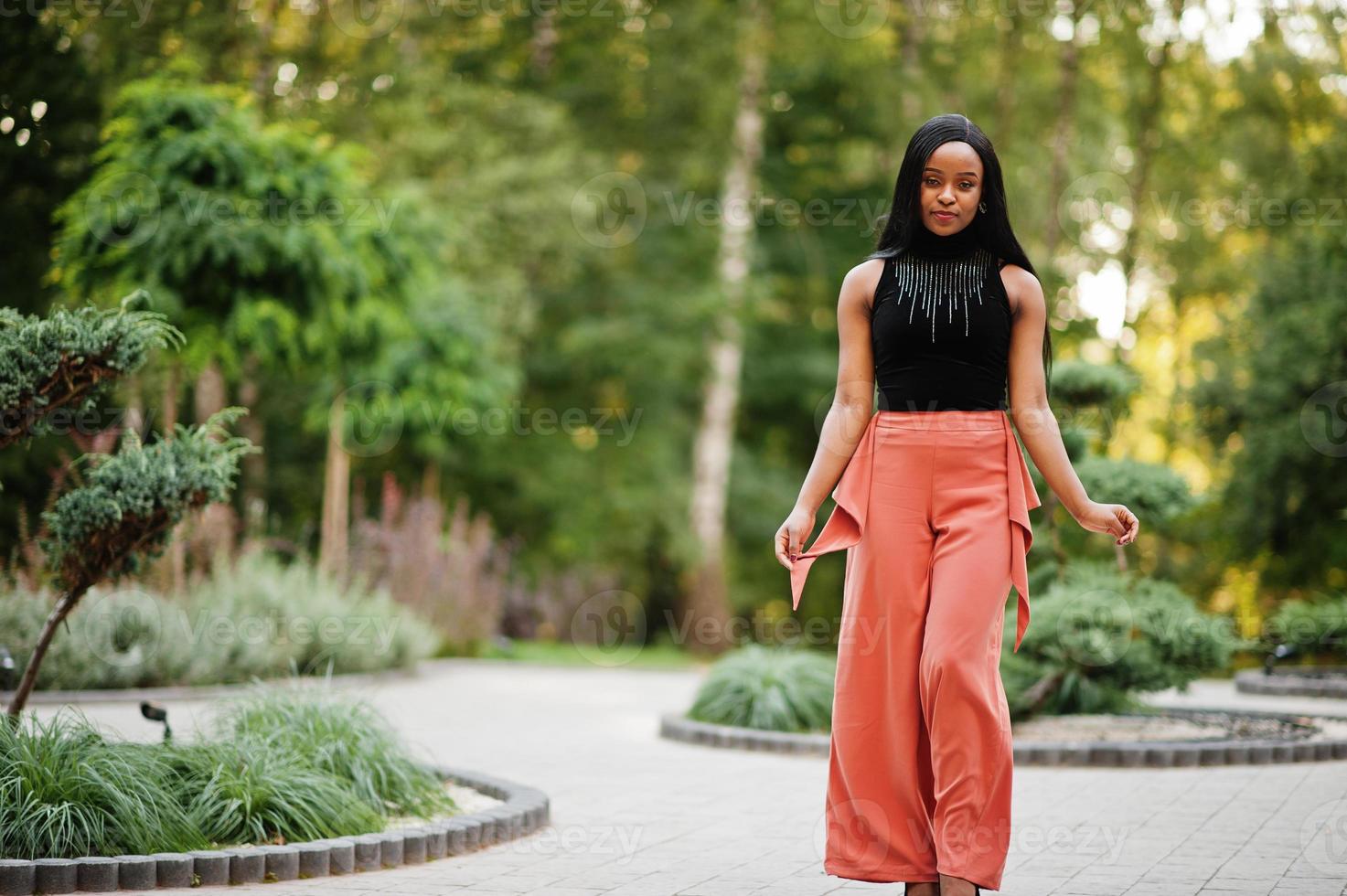 Fashionable african american woman in peach pants and black blouse pose outdoor. photo