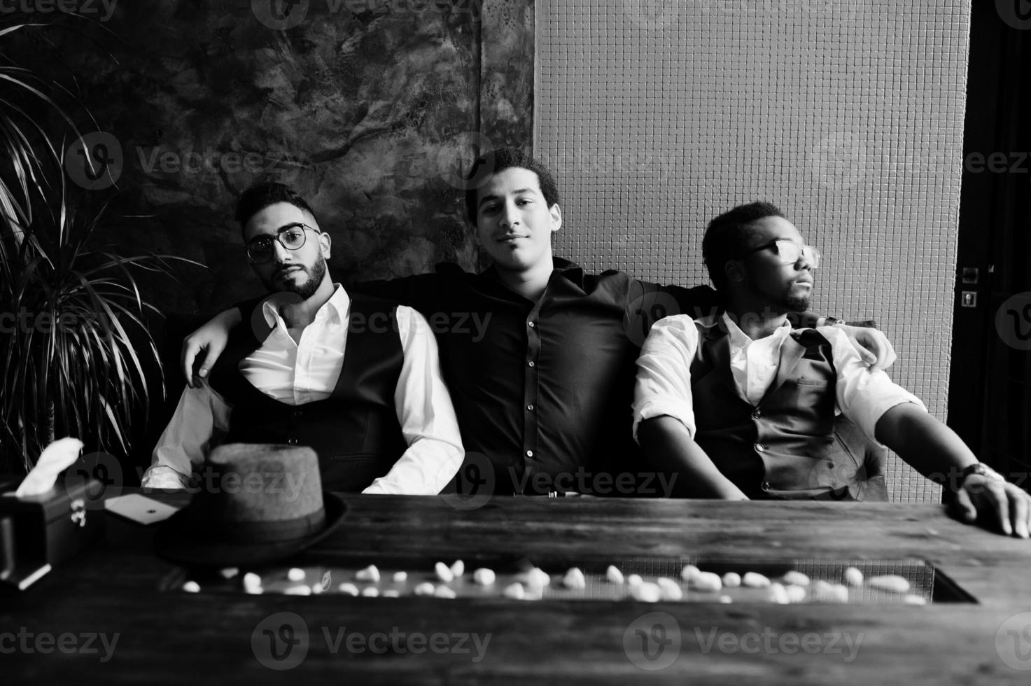 Group of handsome retro well-dressed man gangsters spend time at club. Multiethnic male bachelor mafia party in restaurant, sitting by table. photo