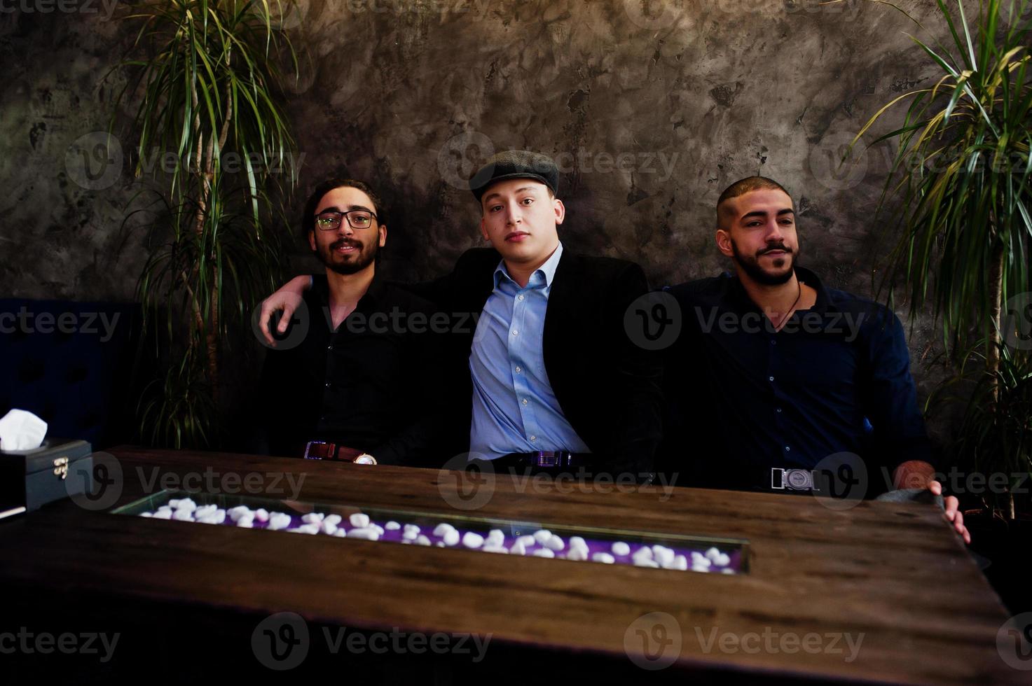 Group of handsome retro well-dressed man gangsters spend time at club. Multiethnic male bachelor mafia party in restaurant, sitting by table. photo