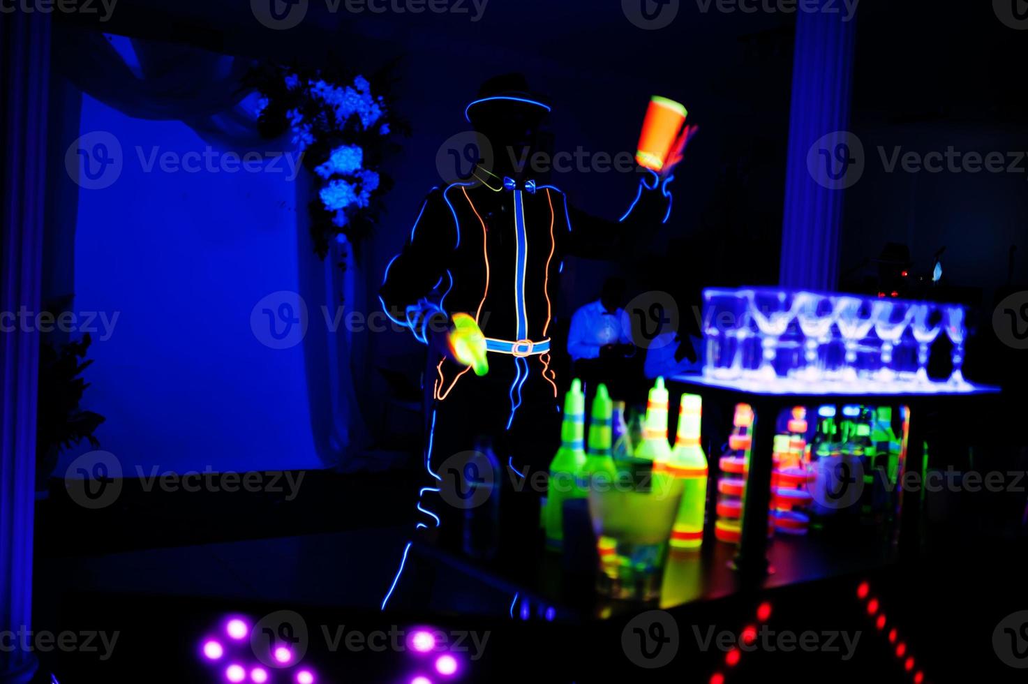 Professional barman and led light show. Silhouette of modern bartender shaking drink at night cocktail bar. photo