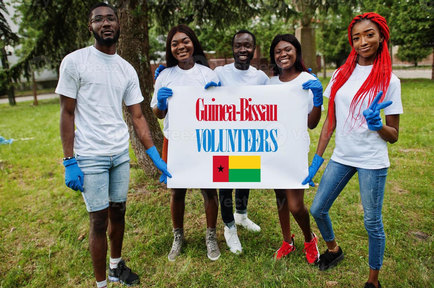 grupo de felices voluntarios africanos se mantienen en blanco con la bandera de guinea-bissau en el parque. Concepto de voluntariado, caridad, personas y ecología de los países africanos. foto