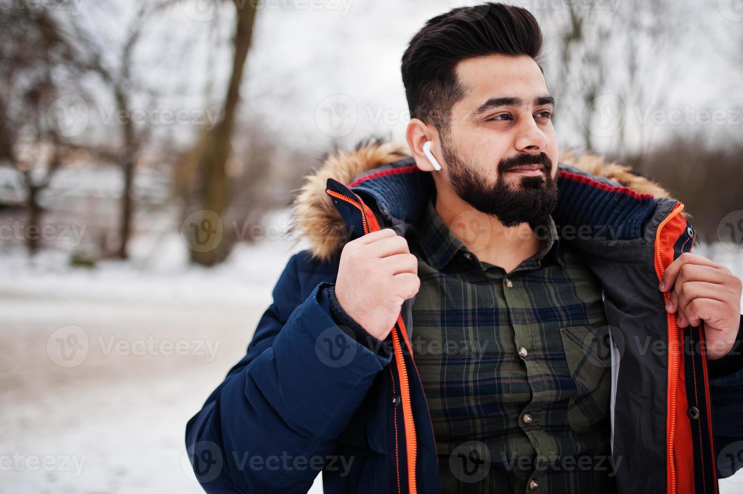 Beard indian man wear jacket in cold winter day. Mobile earphones in ears. photo