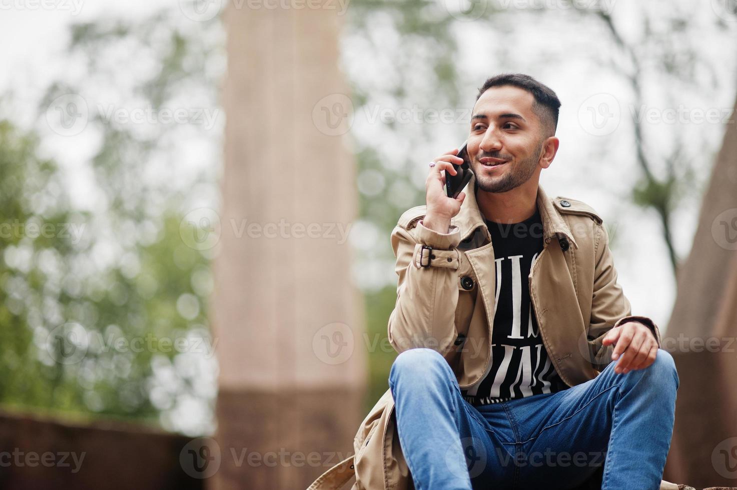 hombre kuwaití con estilo en gabardina con teléfono móvil. foto