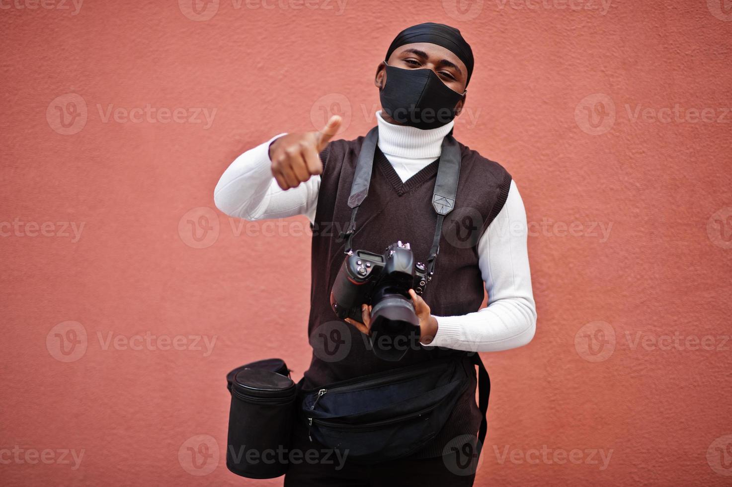 Young professional african american videographer holding professional camera with pro equipment. Afro cameraman wearing black duraq and face protect mask, making a videos. photo