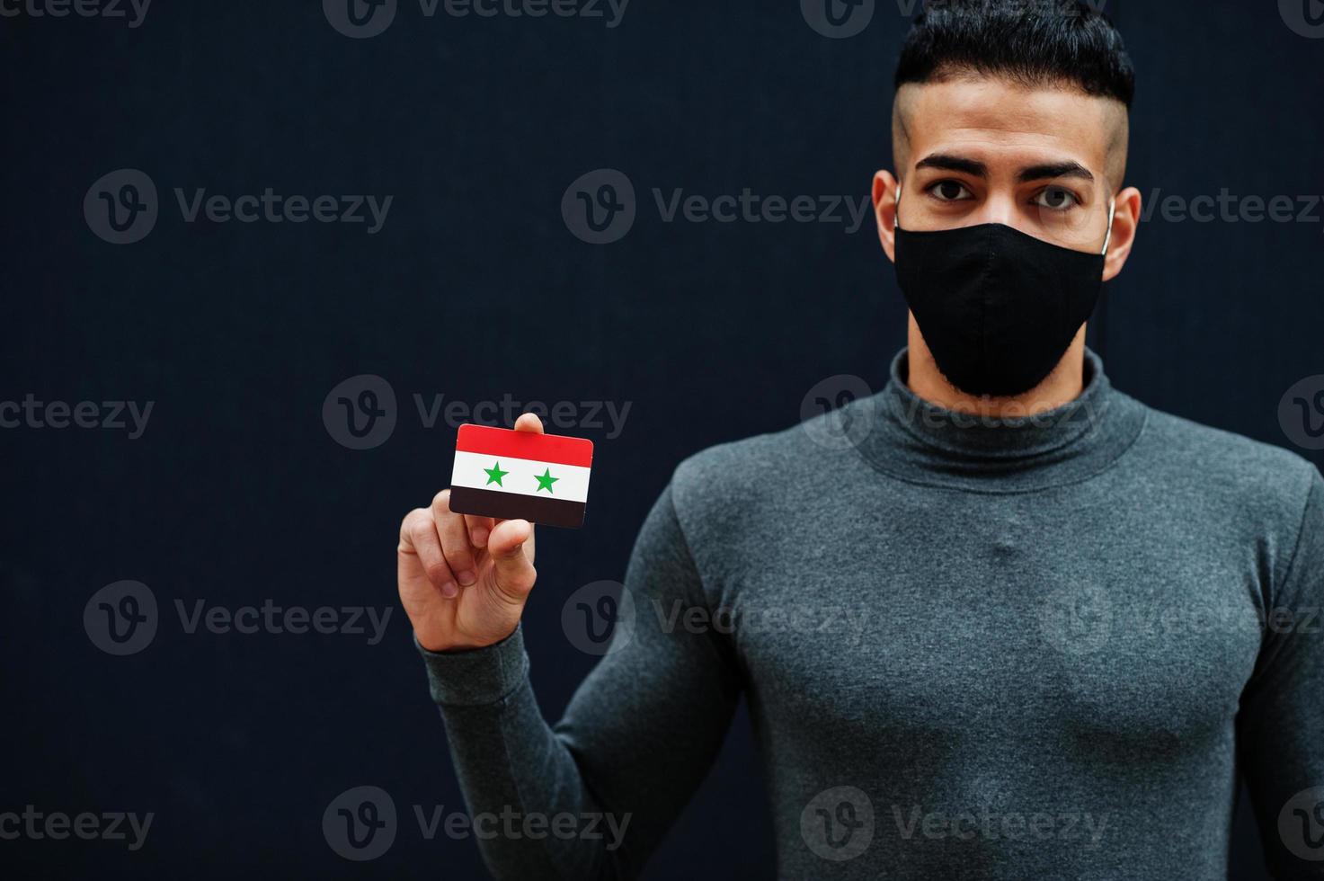 Middle eastern man in gray turtleneck and black face protect mask show Syria flag isolated background. photo