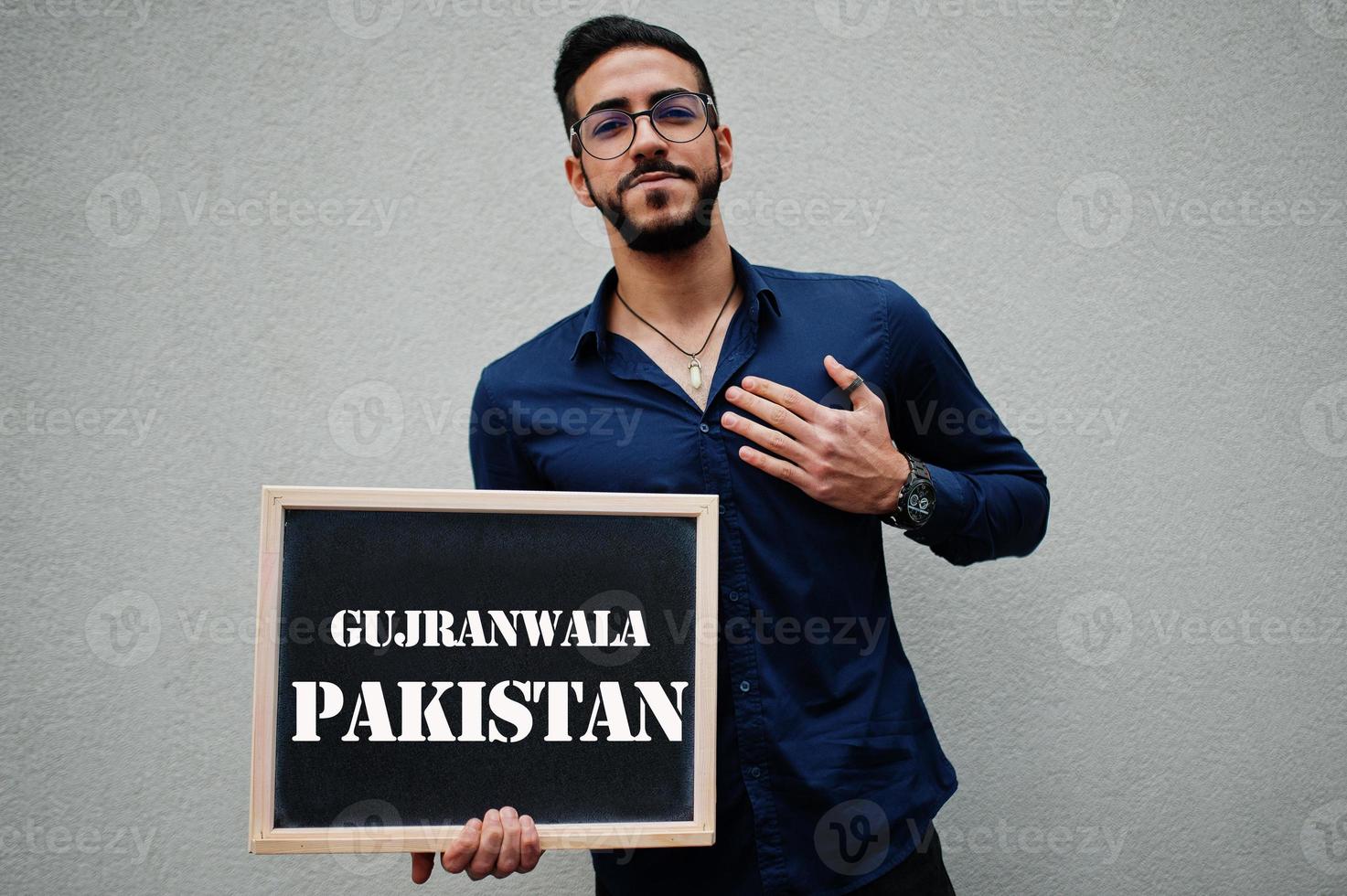 Arab man wear blue shirt and eyeglasses hold board with Gujranwala Pakistan inscription. Largest cities in islamic world concept. photo
