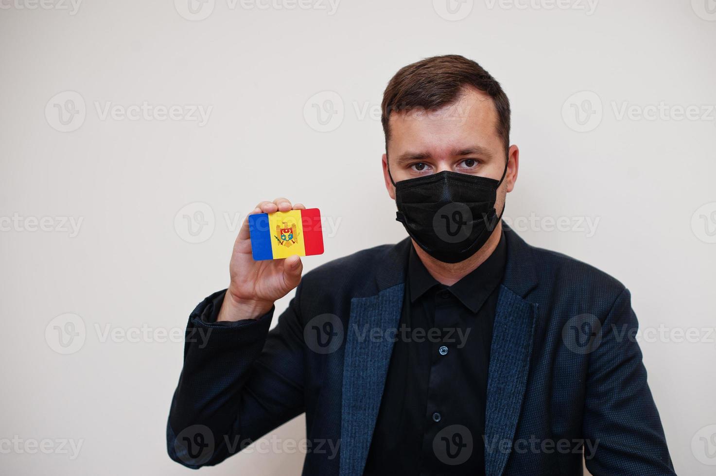 European man wear black formal and protect face mask, hold Moldova flag card isolated on white background. Europe coronavirus Covid country concept. photo
