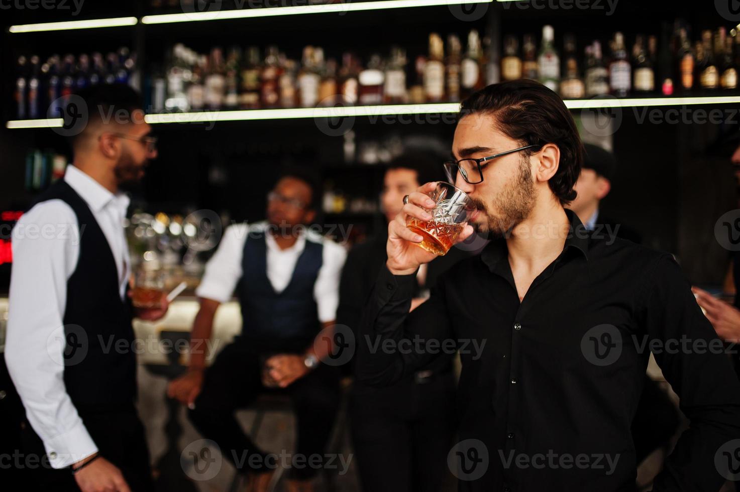 Stylish arab man against group of handsome retro well-dressed guys gangsters spend time at club, drinking on bar counter. Multiethnic male bachelor mafia party in restaurant. photo