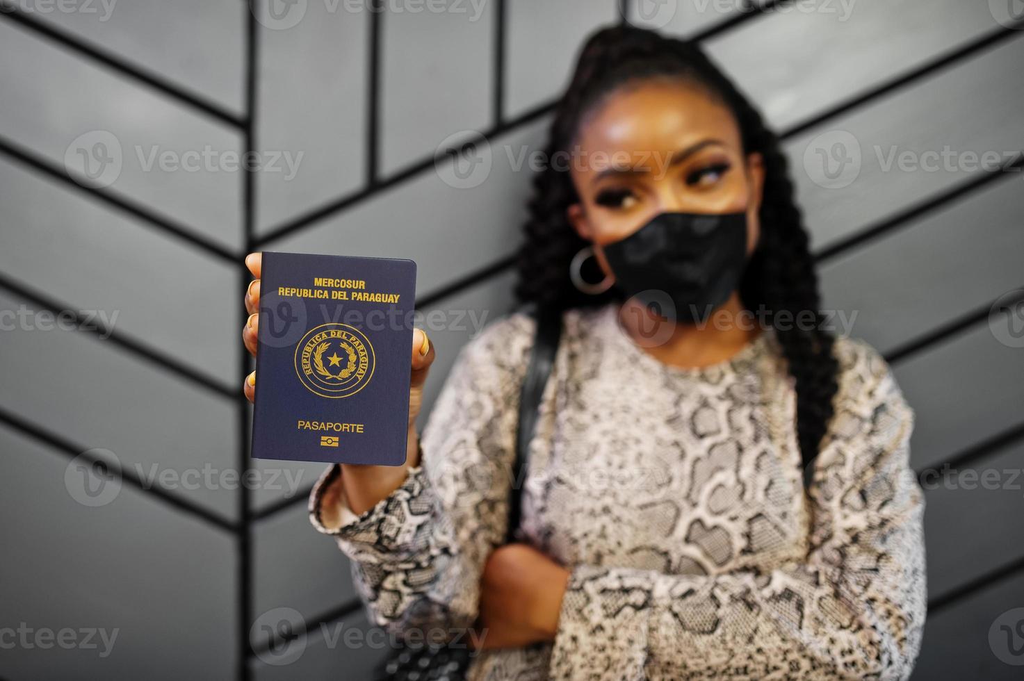 African american woman wearing black face mask show Paraguay passport in hand. Coronavirus in America country, border closure and quarantine, virus outbreak concept. photo
