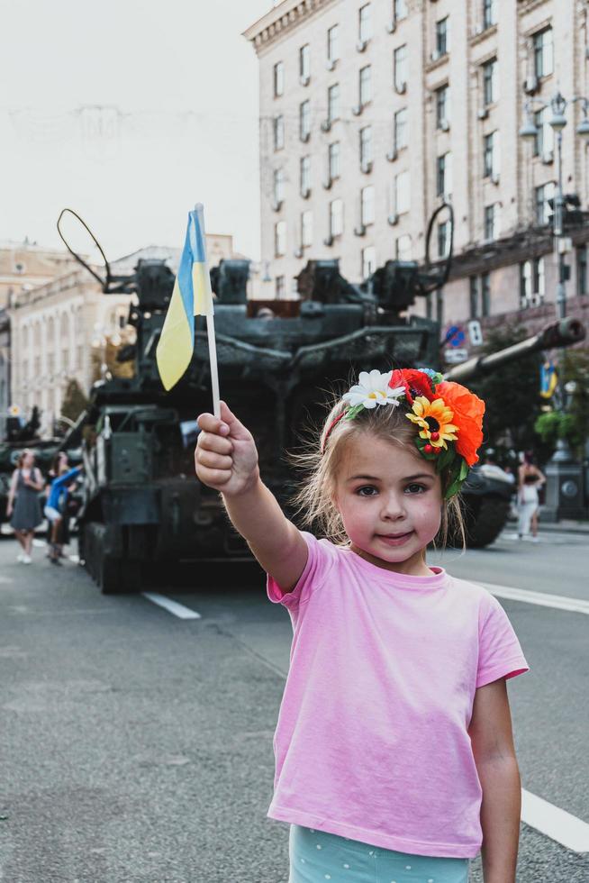 Kyiv, Ukraine - 23 August 2022. Little Ukrainian girl with flag in her hand posing near destroyed tank. photo