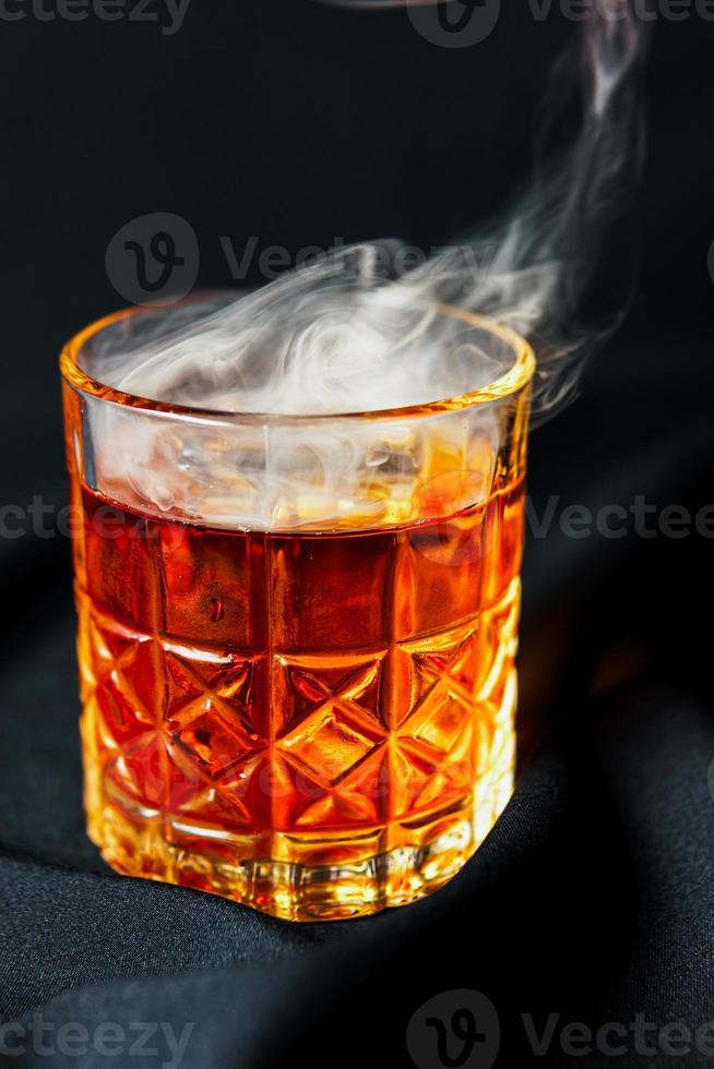 Alcoholic drink. A cocktail with whiskey or cognac with fire and smoke close-up, dark black background photo