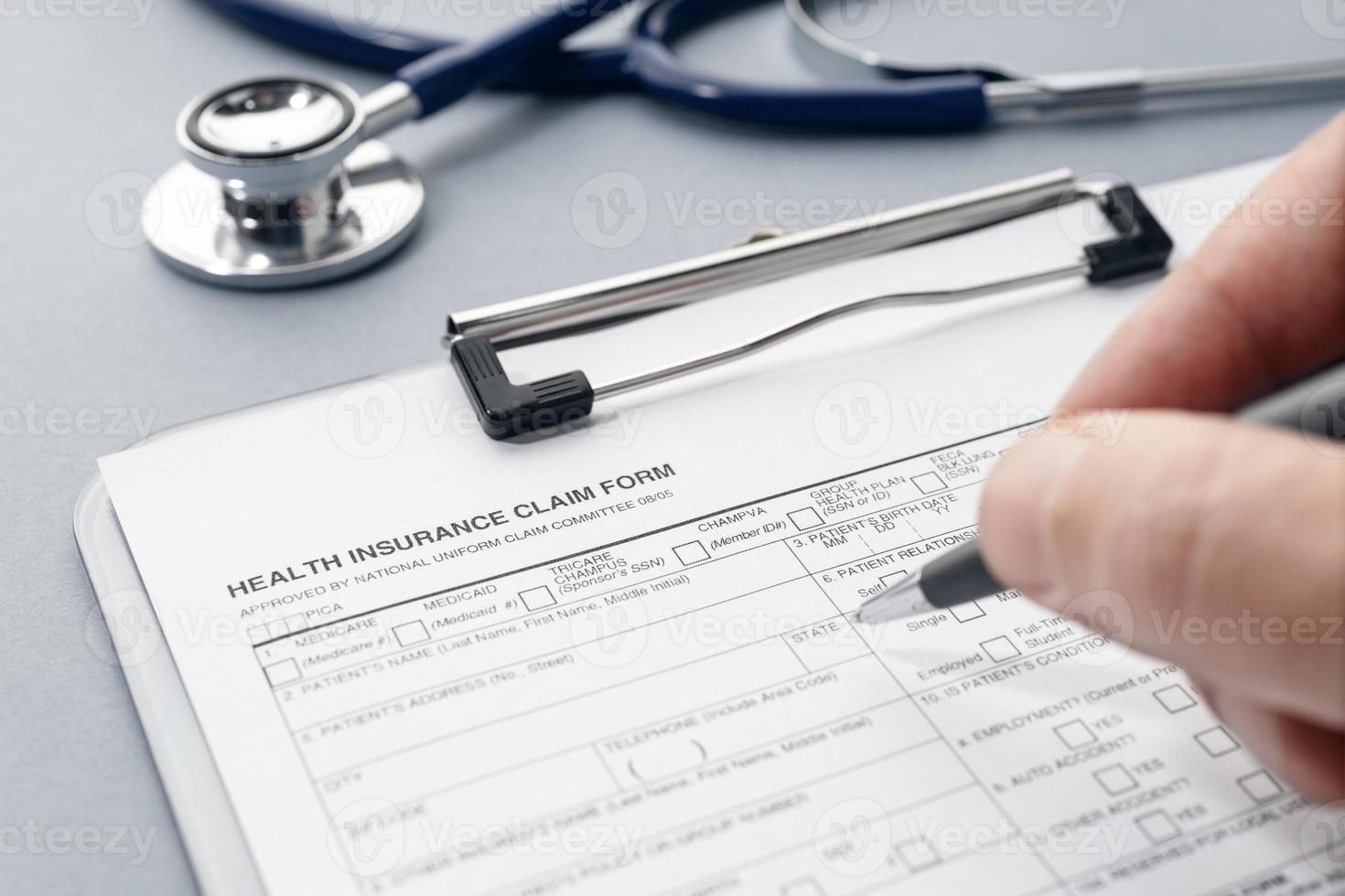 Hand filling on Health Insurance claim form and stethoscope on desk photo