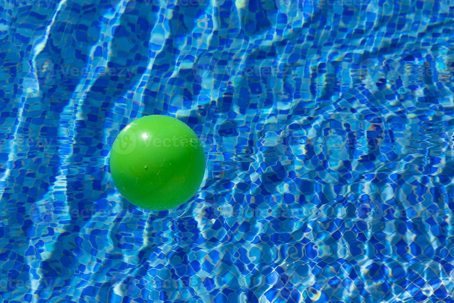 Round green ball on the surface of the water in a pool with blue water and waves. The concept of children's safety near the water. photo