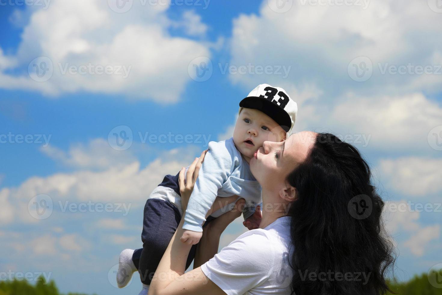 Happy young girl, mom plays with her baby in her arms against a background of blue sky with clouds. Copy space. photo