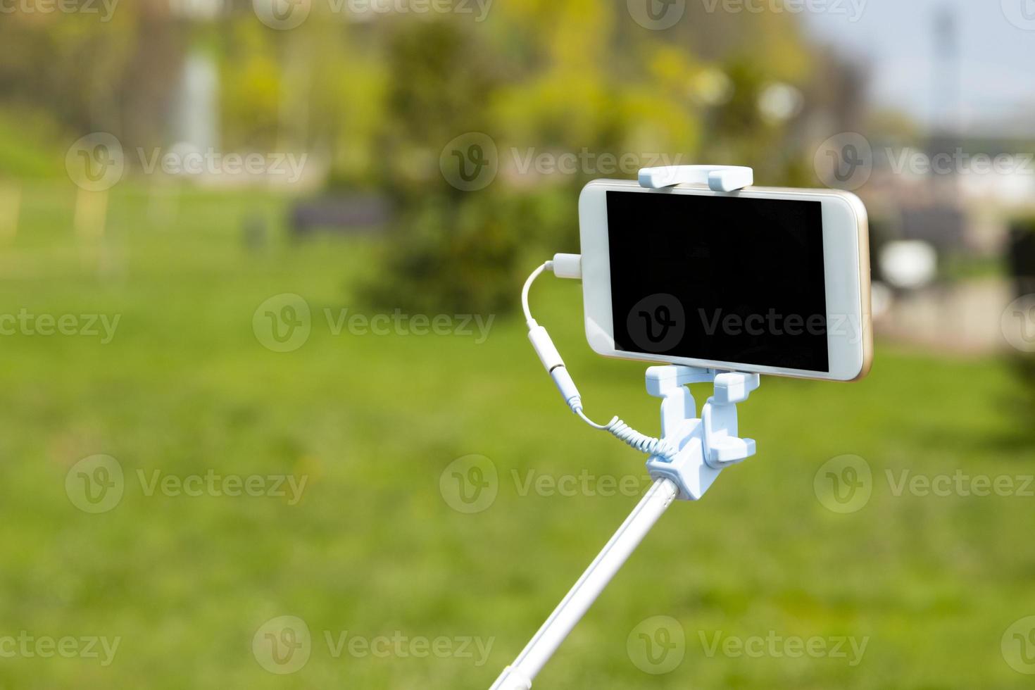 Taking pictures with smart phone with selfie stick on blurred beautiful background, vacation concept. Copy space. photo