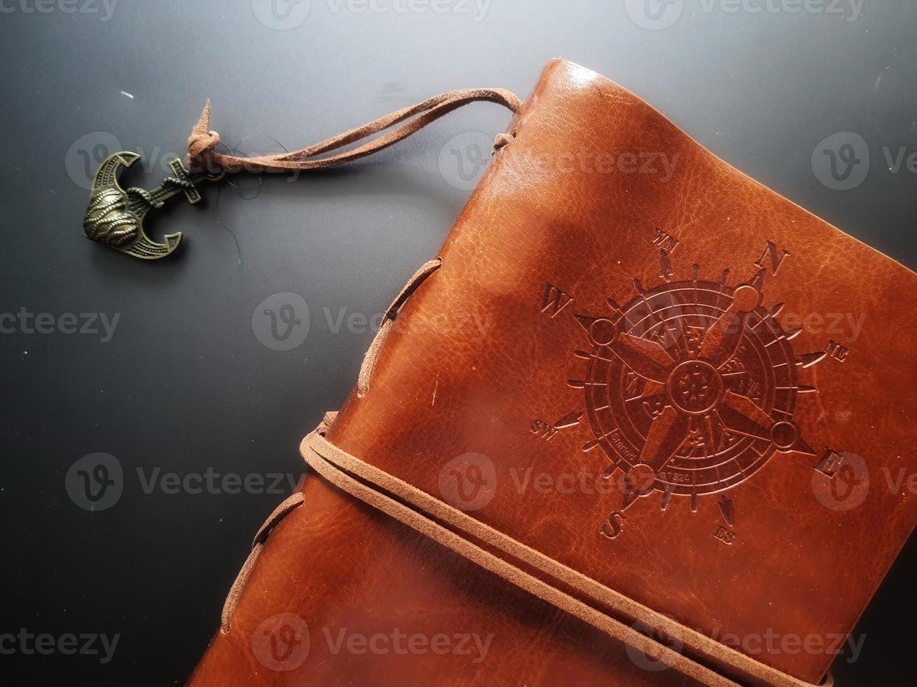 A notebook with a brown leather cover with a compass motif and anchor strap. photo