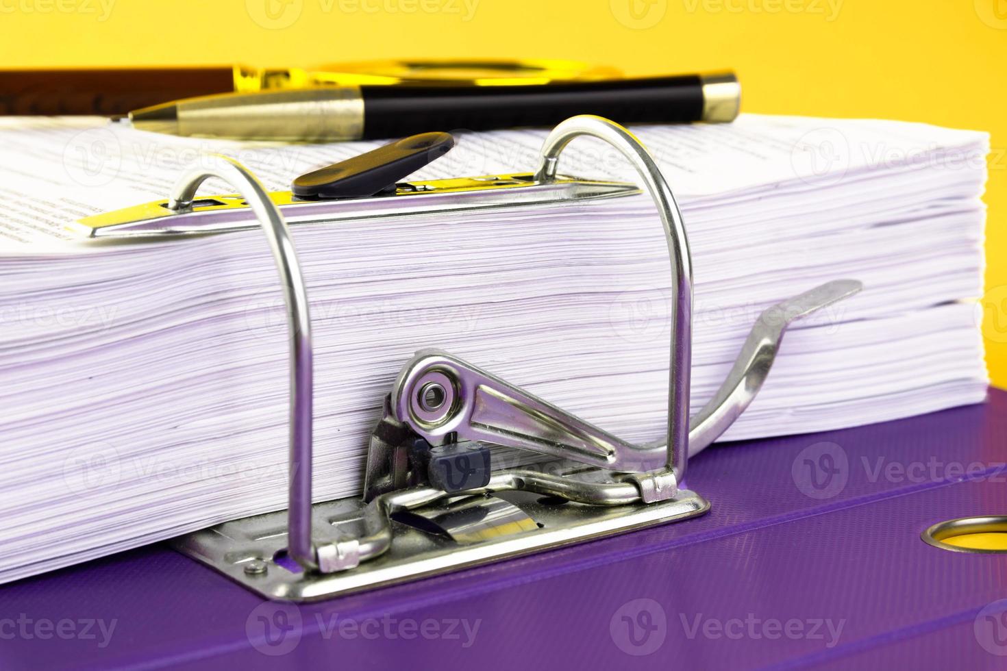 Close up of a pile of unfinished documents awaiting verification, a magnifying glass, on a yellow background. Business and education concept. Copy space photo