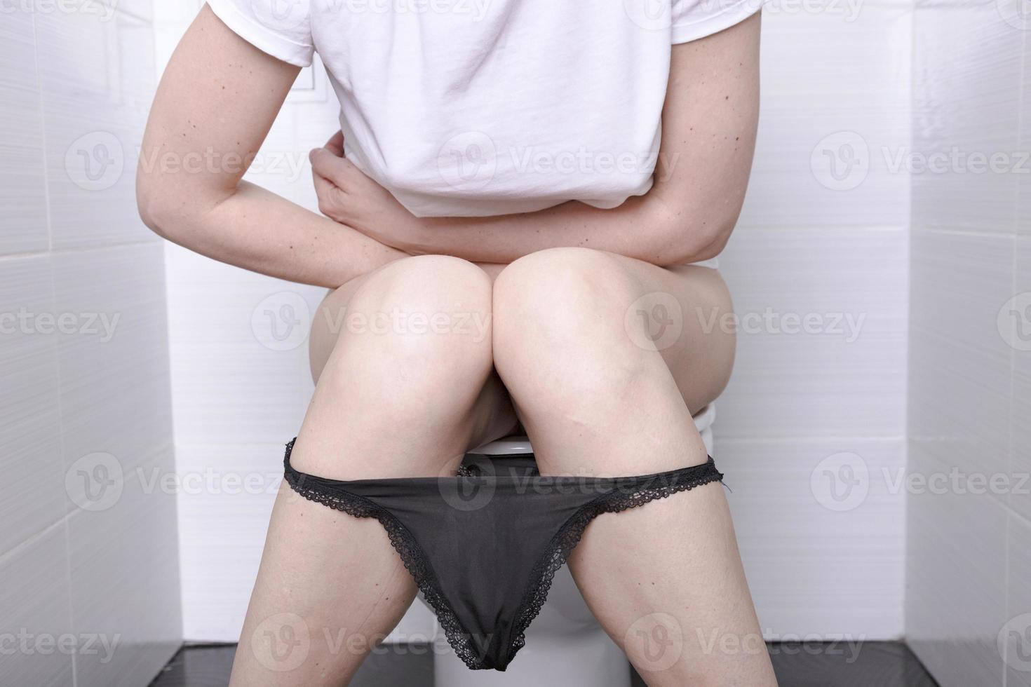 Pissing Woman, with diarrhea on a white toilet bowl in the toilet with a roll of paper in her hand. photo