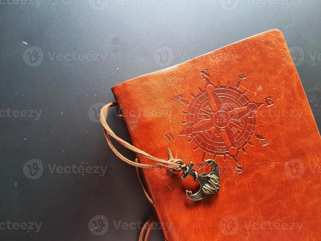 A notebook with a brown leather cover with a compass motif and anchor strap. photo