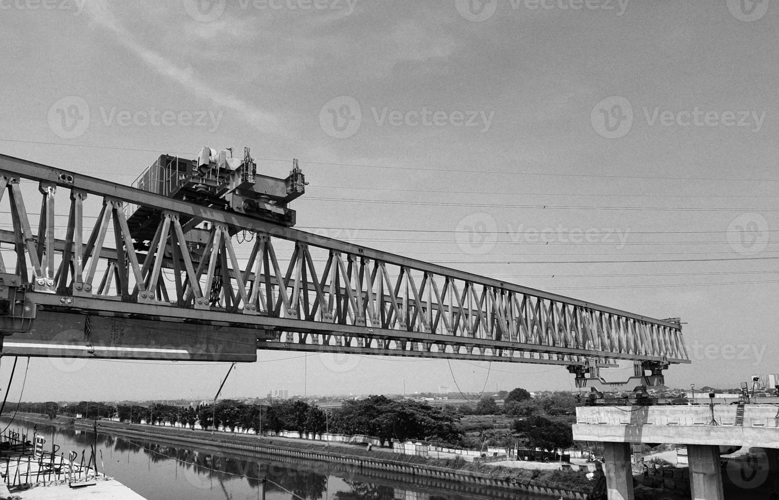 Black and white photo of the steel structure of a launcher gantry that will be used for erection precast concrete I Girder across the river .  This yellow gantry launcher comes from China.