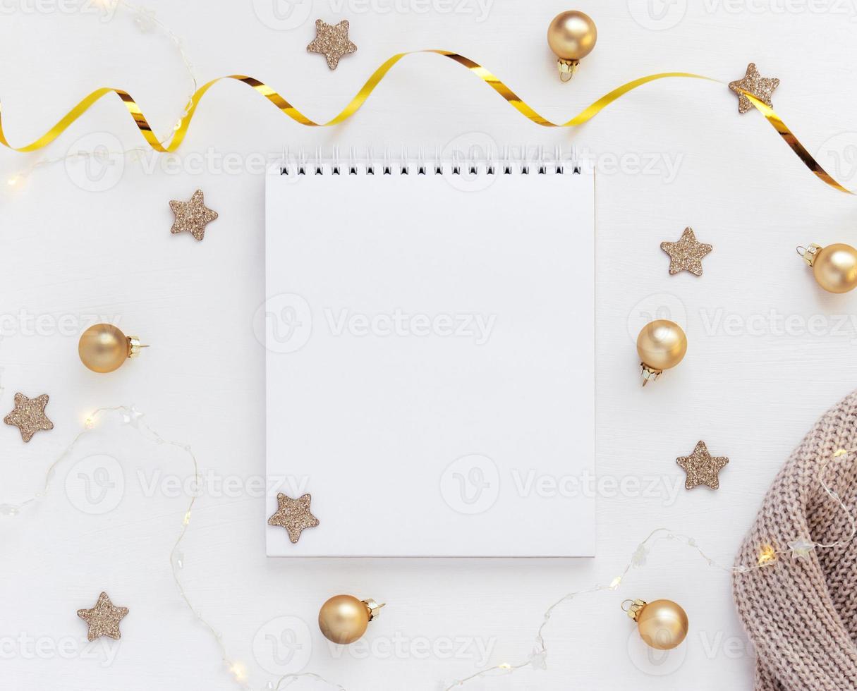 White sheet of notebook on white table with stars, Christmas balls and festive garland. Concept planning, wish list for the new year photo