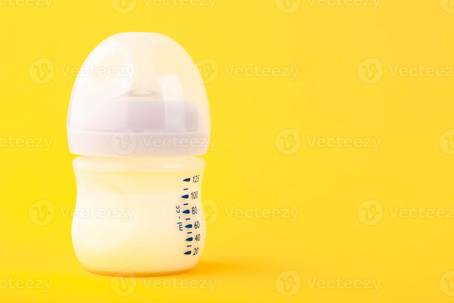 White plastic baby bottle with pacifier, rich in baby food, on yellow background. Copy space. photo