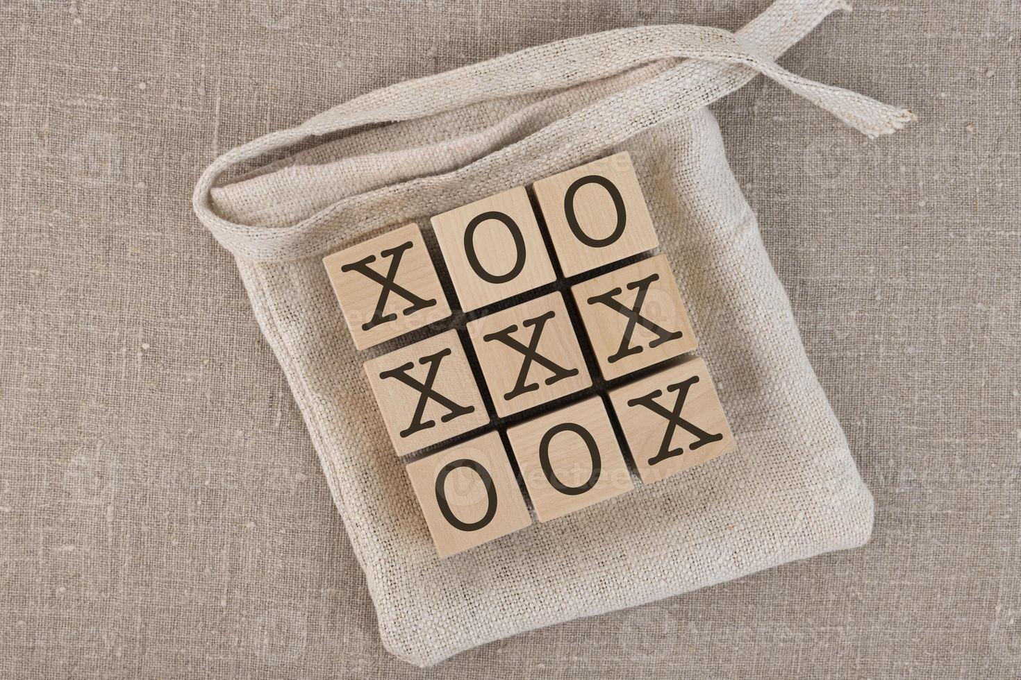 Bloques de madera de tres en raya con bolsa. jugar sobre un fondo de lino gris, también conocido como tic-tac-toe. foto