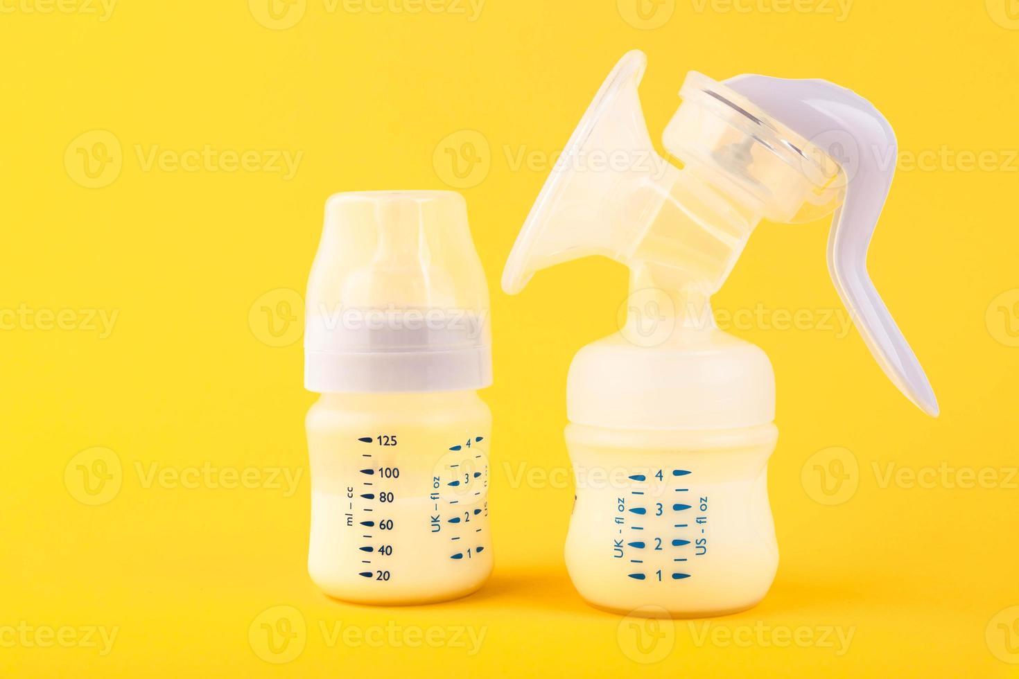 White plastic baby bottle with pacifier,breast pump rich in baby food, on yellow background. Copy space. photo