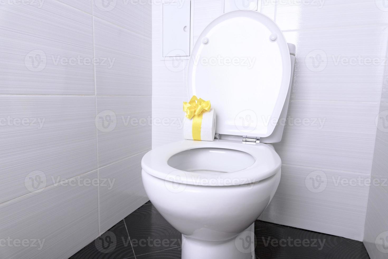 White home toilet with flush and white toilet paper with a gift yellow bow in the bathroom. Quarantine concept. photo