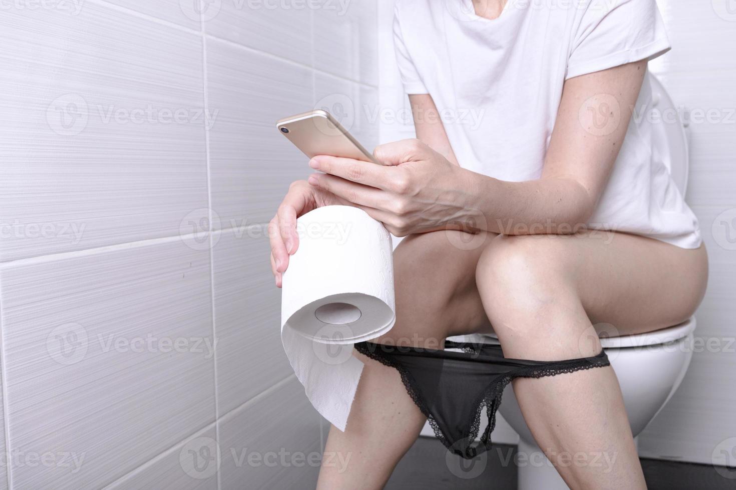 A beautiful girl is sitting on the toilet. Woman in panties relaxing on the toilet with the phone. Pensive teenage girl sits with panties on the toilet. photo