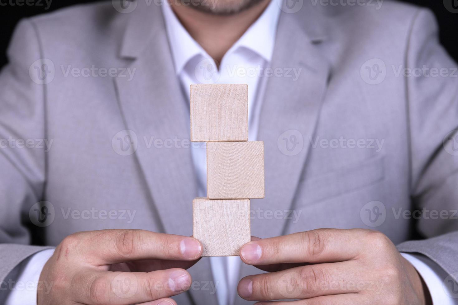 Businessman stacks wooden cube blocks in pyramid with empty space for icons photo