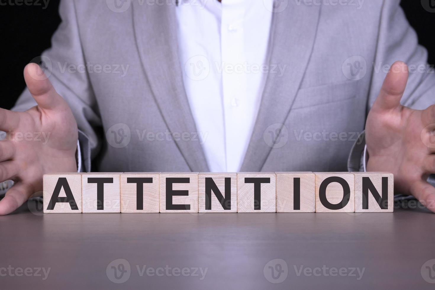 ATTENTION, the word is written on wooden cubes, blocks on the background of a man, a businessman in a gray suit. Focus on the point. Self-discipline and perseverance. photo