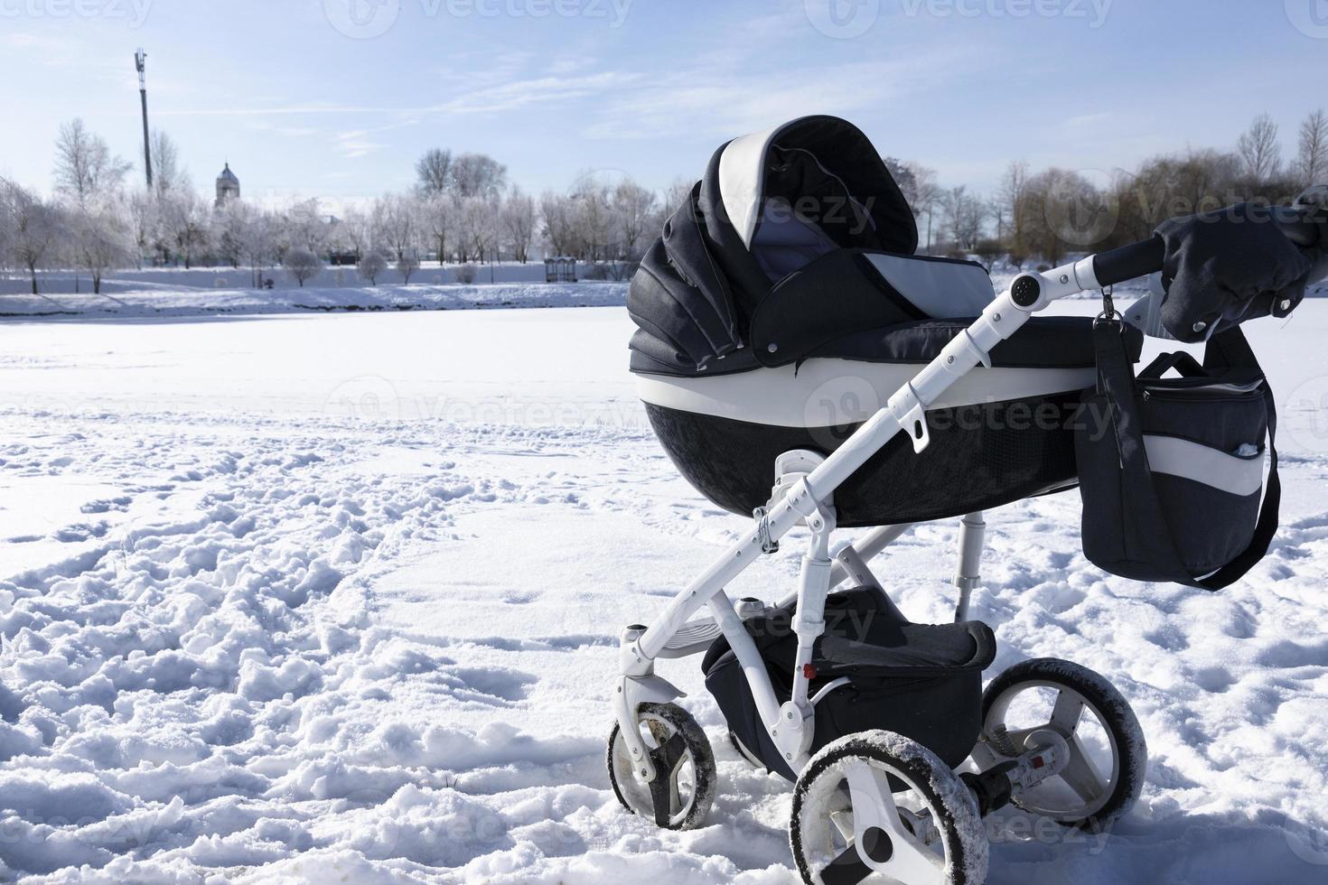 carro de bebé en el lago en el parque en invierno. playa bajo la nieve. el concepto de vacaciones de invierno, caminar con niños. foto