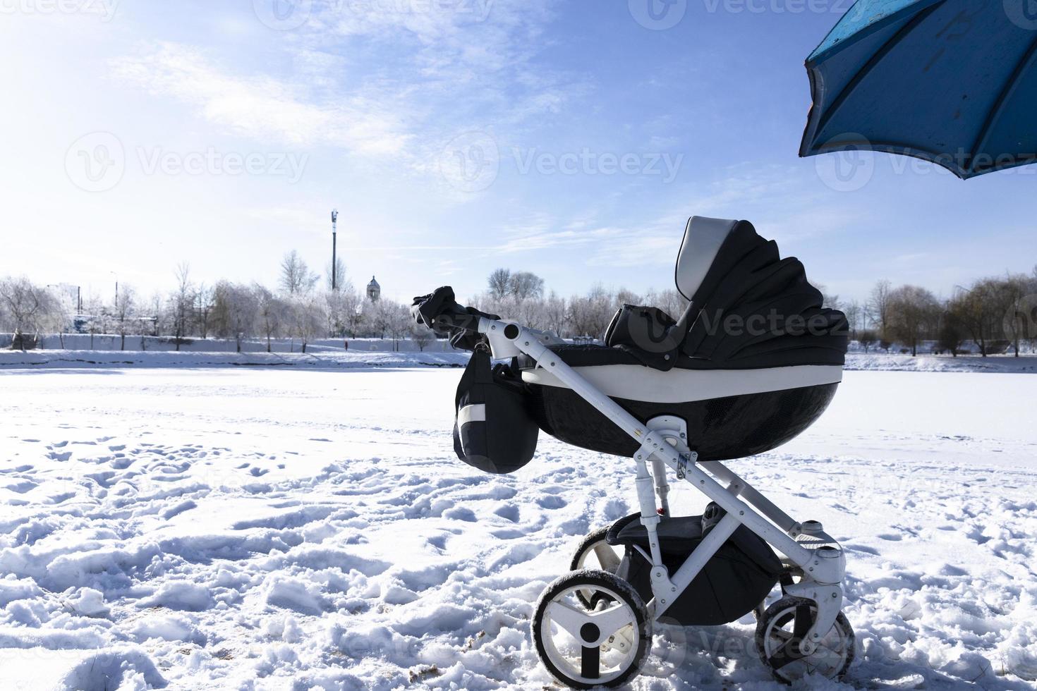 carro de bebé en el lago en el parque en invierno. playa bajo la nieve. el concepto de vacaciones de invierno, caminar con niños. foto