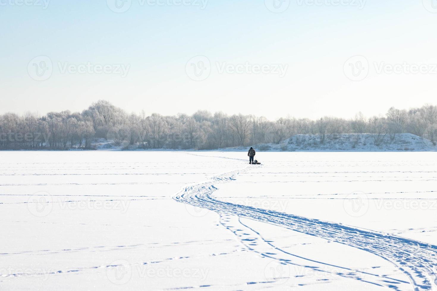 A lonely old hermit, in winter, crosses the river on ice and pulls a sled with firewood for heating photo