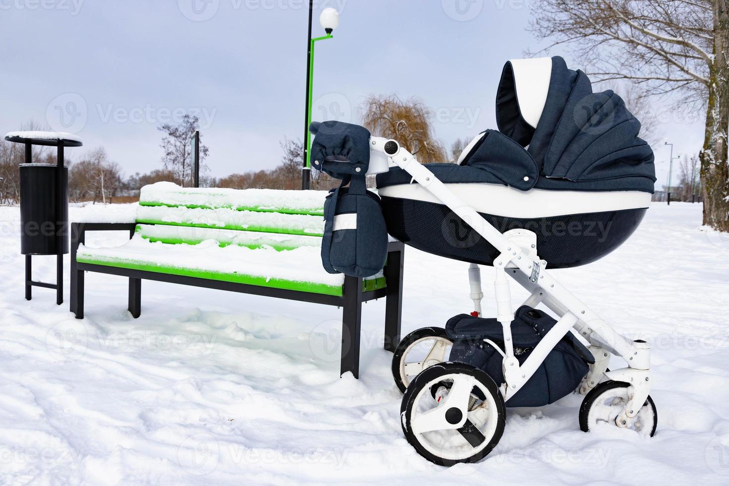 el niño duerme en un cochecito. un cochecito de bebé se encuentra en el parque junto al banco en invierno. foto